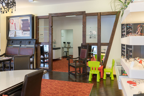 Modernes Optiker-Geschäft mit Brillenregalen, Kinderspielecke und stilvollen Sitzmöbeln.