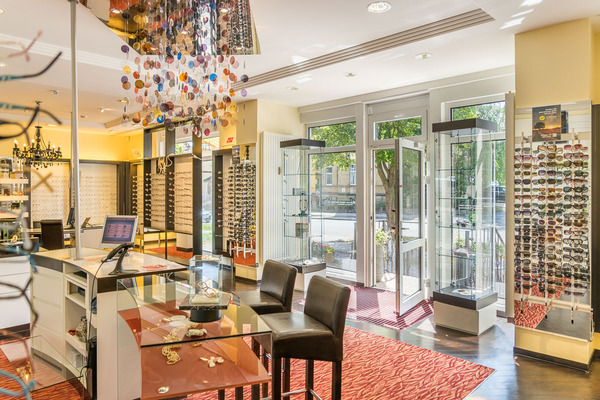 Heller Optikerladen mit modernen Brillen, Sonnenbrillen und Schmuck auf Glasvitrinen.